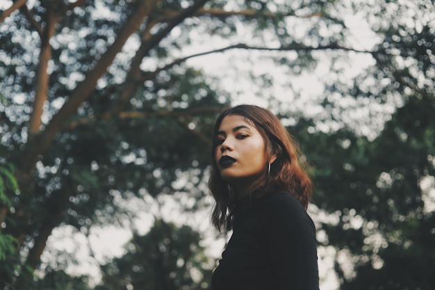 Mulher bonita de vestido preto em pé na floresta.