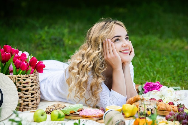 Foto mulher bonita descansando no parque sentada em um cobertor de piquenique com frutas e vinho