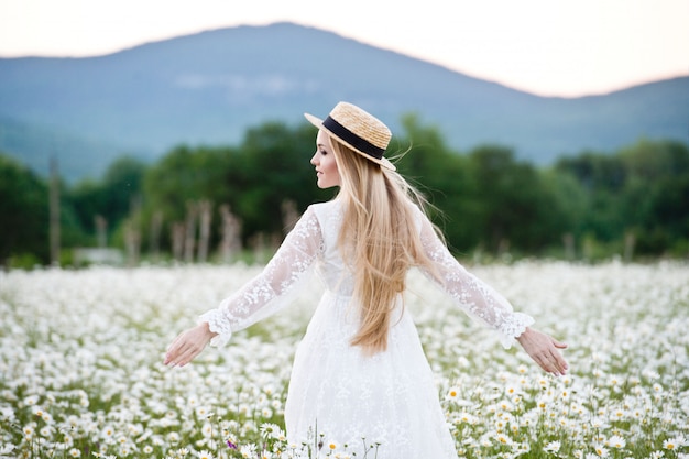 Foto mulher bonita, desfrutando de campo de margarida. mulher loira com chapéu de palha e buquê.