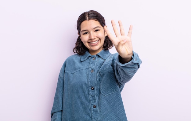 Mulher bonita e adolescente sorrindo e parecendo amigável, mostrando o número quatro ou o quarto com a mão para a frente, em contagem regressiva