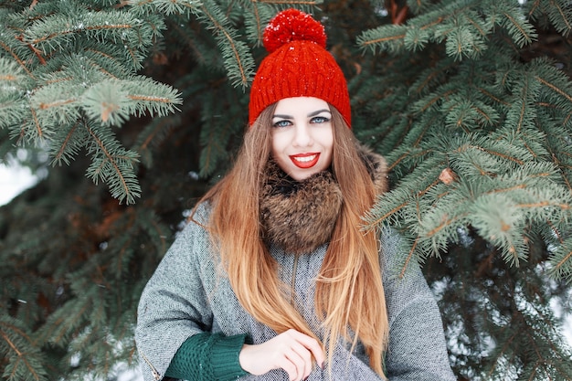Mulher bonita e alegre com roupas elegantes de inverno em pé perto de um abeto vermelho