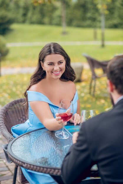 Mulher bonita e alegre em um vestido com ombros nus sentada com o vidro estendido e o homem em frente