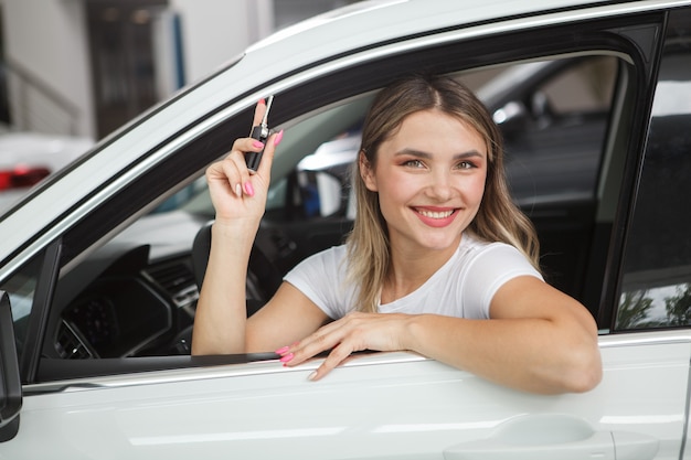 Mulher bonita e alegre segurando as chaves do carro, sentada em seu novo automóvel