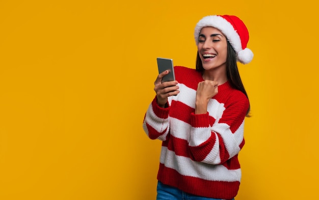 Mulher bonita e animada aos gritos com o smartphone nas mãos por ter ganhado algum presente na época do Natal