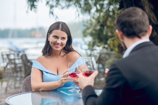 Mulher bonita e bem cuidada e homem com lindas roupas com taças de vinho, conversando em um café ao ar livre