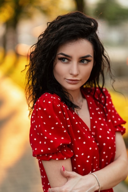 Mulher bonita e bonita encaracolada com um lindo rosto feminino em um vestido vermelho na rua