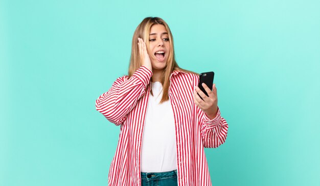 Mulher bonita e curvilínea se sentindo feliz, animada e surpresa, segurando um telefone inteligente