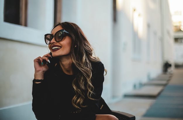 Mulher bonita e elegante com óculos de sol, falando ao telefone. menina sentada com telefone celular.