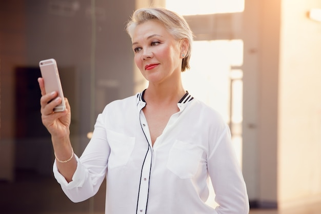 Foto mulher bonita e elegante de meia-idade com cabelos grisalhos usando smartphone