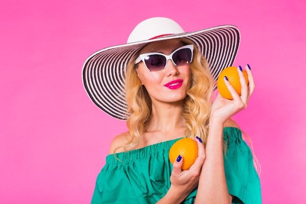 Mulher bonita e elegante em óculos escuros e chapéu com laranjas