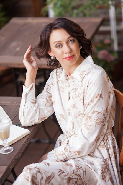 Mulher bonita e elegante em um vestido bege, bebendo café ao ar livre no café.