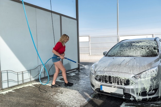 Mulher bonita e esportiva lavando carros com espuma na lavagem de carros