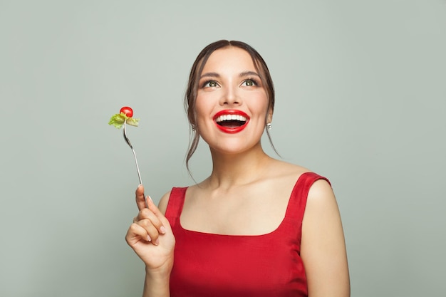 Foto mulher bonita e feliz comendo comida saudável segurando um garfo com tomates e alface em fundo branco conceito de alimentação e dieta saudável