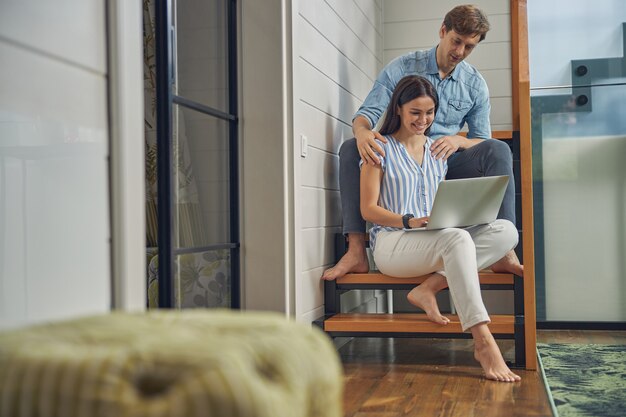 Mulher bonita e homem bonito passando um tempo no laptop enquanto estão sentados nas escadas de uma casa moderna