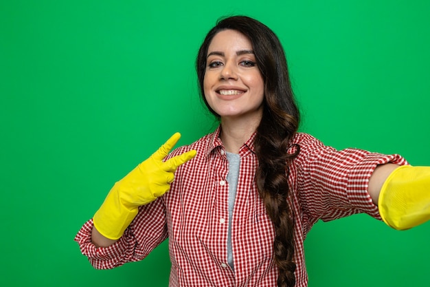 Mulher bonita e limpadora caucasiana sorridente com luvas de borracha segurando, olhando e gesticulando sinal de vitória