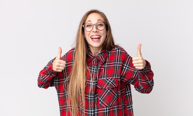 Mulher bonita e magra com um sorriso largo, parecendo feliz, positiva, confiante e bem-sucedida, com os dois polegares para cima