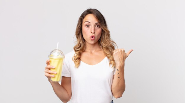 Mulher bonita e magra parecendo espantada com a descrença e segurando um milkshake de baunilha