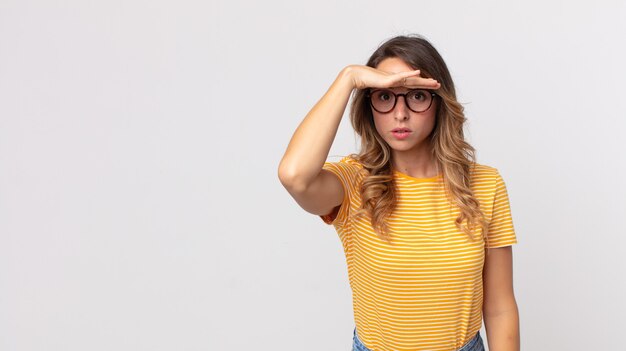 Mulher bonita e magra parecendo perplexa e atônita, com a mão na testa olhando para longe, observando ou procurando