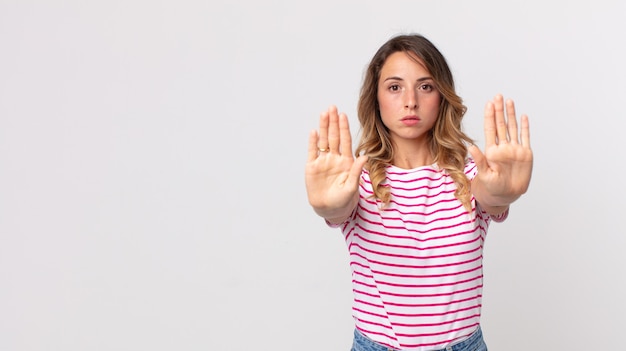 Mulher bonita e magra parecendo séria, infeliz, irritada e descontente, proibindo a entrada ou dizendo pare com as palmas das mãos abertas