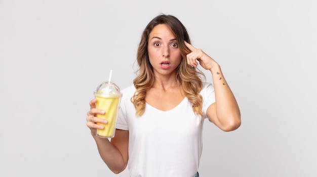 Mulher bonita e magra parecendo surpresa, percebendo um novo pensamento, ideia ou conceito e segurando um milkshake de baunilha