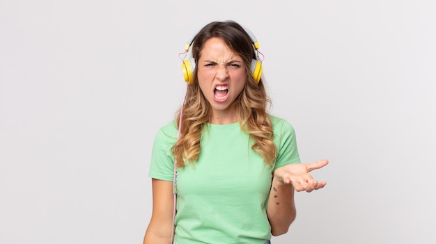 Mulher bonita e magra parecendo zangada, irritada e frustrada ouvindo música com fones de ouvido