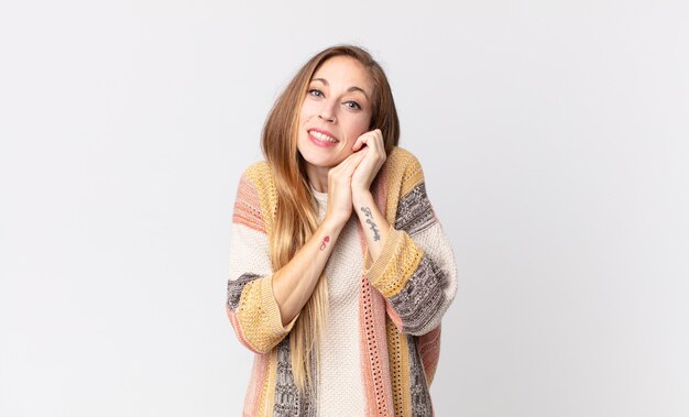 Mulher bonita e magra se sentindo apaixonada e bonita, adorável e feliz, sorrindo romanticamente com as mãos ao lado do rosto