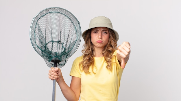 Mulher bonita e magra se sentindo mal, mostrando os polegares para baixo, usando um chapéu e segurando uma rede de pesca