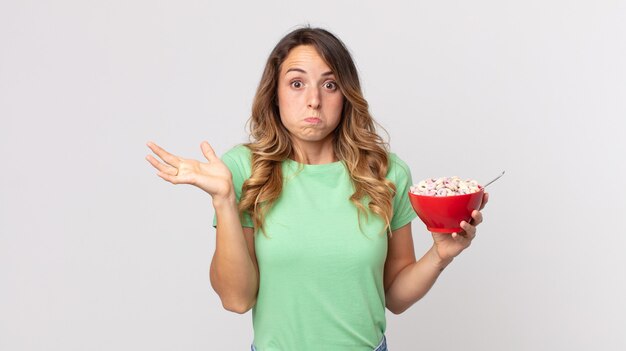 Mulher bonita e magra se sentindo perplexa e confusa, duvidando e segurando uma tigela de café da manhã