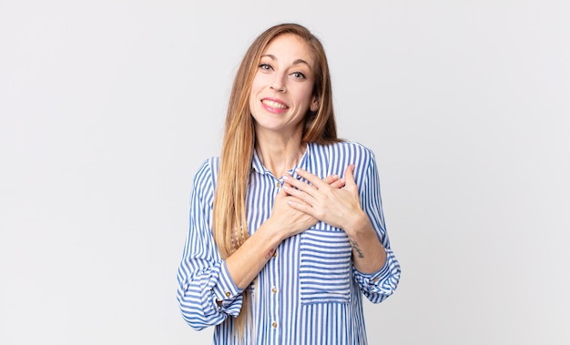 Mulher bonita e magra se sentindo romântica, feliz e apaixonada, sorrindo alegremente e segurando o coração de mãos dadas