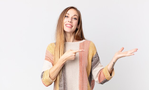 Mulher bonita e magra sorrindo alegremente e apontando para copiar o espaço na palma da mão ao lado, mostrando ou anunciando um objeto