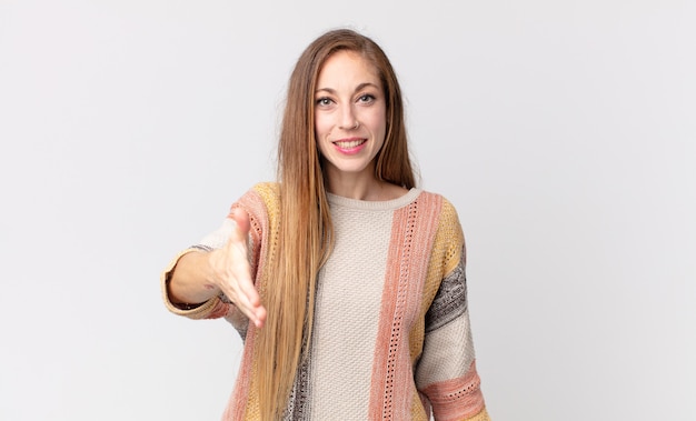 Mulher bonita e magra sorrindo, parecendo feliz, confiante e amigável, oferecendo um aperto de mão para fechar um negócio, cooperando