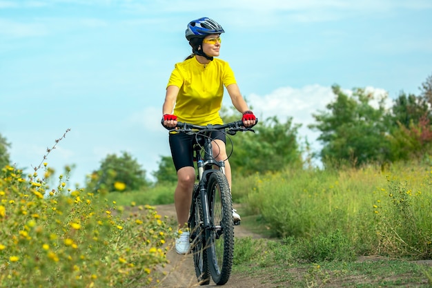 Mulher bonita em amarelo andando de bicicleta na natureza