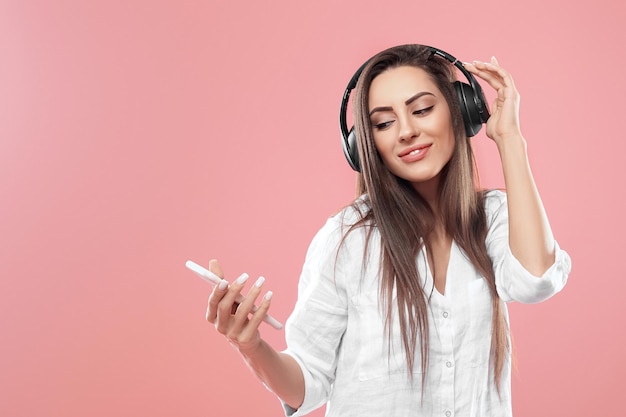 Mulher bonita em fones de ouvido com smartphone ouvindo música sobre fundo rosa