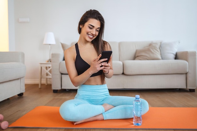 Mulher bonita em fones de ouvido olhando para smartphone ouvindo música e relaxando após o treino