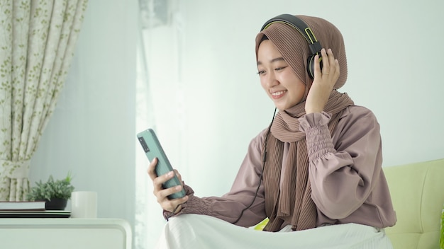 Mulher bonita em hijab ouvindo música divertida em seu smartphone em casa