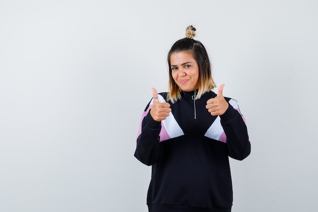 Mulher bonita em moletom mostrando os polegares para cima e parecendo satisfeita