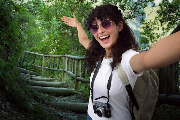 Mulher bonita em óculos de sol com câmera tirando selfie nas escadas nas montanhas