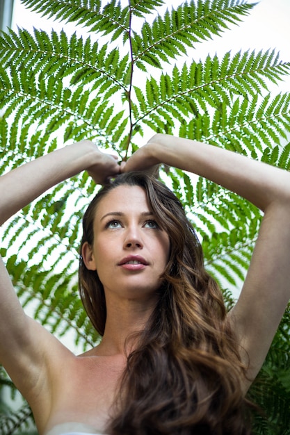 Foto mulher bonita em pé ao ar livre contra plantas verdes com as mãos na cabeça