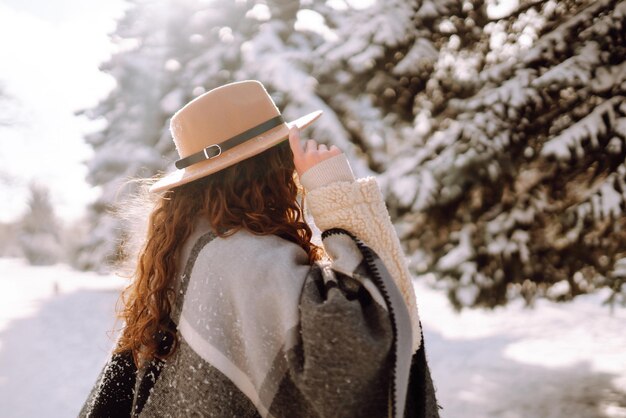 Mulher bonita em pé entre árvores nevadas e curtindo a primeira neve. Tempo feliz. Natal.