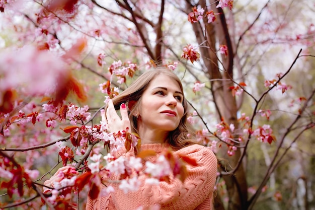 Mulher bonita em pé sob a árvore de flor rosa no parque primavera