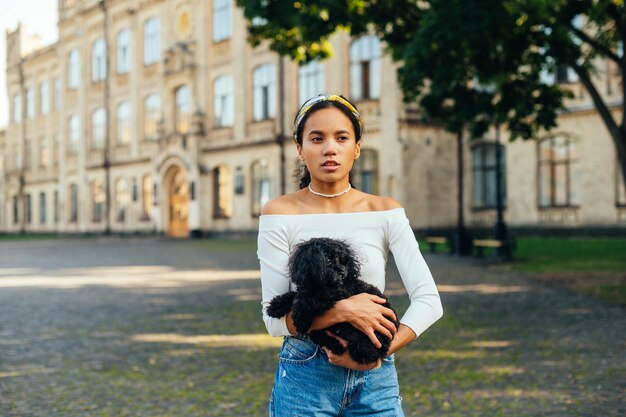 Mulher bonita em roupas elegantes fica no parque e segura um cachorrinho preto