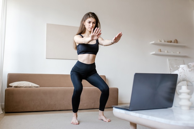 Mulher bonita em roupas esportivas fazendo exercícios de ioga, mantendo um estilo de vida saudável e usando laptop