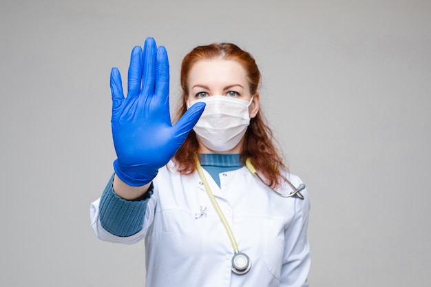 Foto mulher bonita em roupas médicas brancas, máscara, luvas azuis e estetoscópio nos ombros, imagens isoladas em fundo cinza