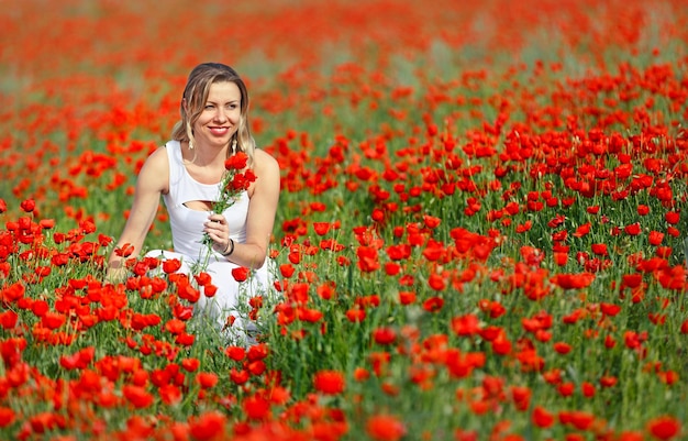 Mulher bonita em um campo de flores de papoula vermelhas brilhantes no verão