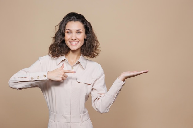 Mulher bonita em um fundo bege sorri e ri faz um gesto com as mãos para a venda e promoção lateral