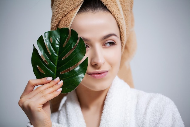 Mulher bonita em um jaleco branco com uma toalha na cabeça e pele clara segura uma folha verde.