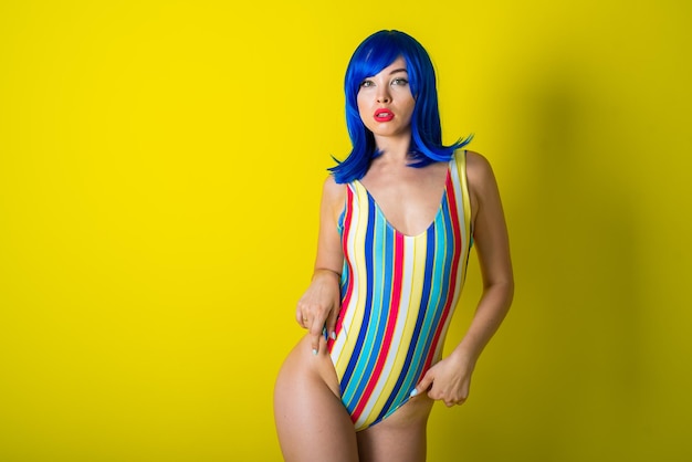 Mulher bonita em um maiô listrado em uma peruca azul posando em um fundo amarelo Retrato de uma garota glamourosa