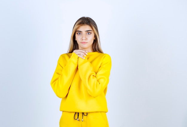 Mulher bonita em um moletom amarelo em pé e posando sobre uma parede branca