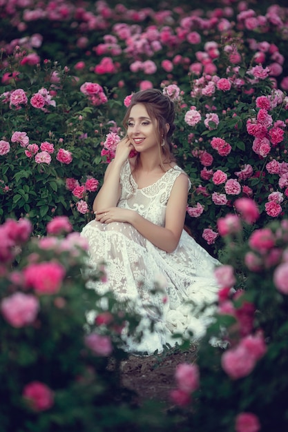 Mulher bonita em um parque floral, rosas do jardim. maquiagem, cabelo, uma coroa de rosas. vestido de noiva longo. mulher no estilo boho