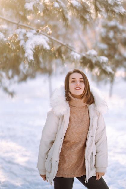 Mulher bonita em um parque nevado. Jovem caminhando em um dia ensolarado de inverno.